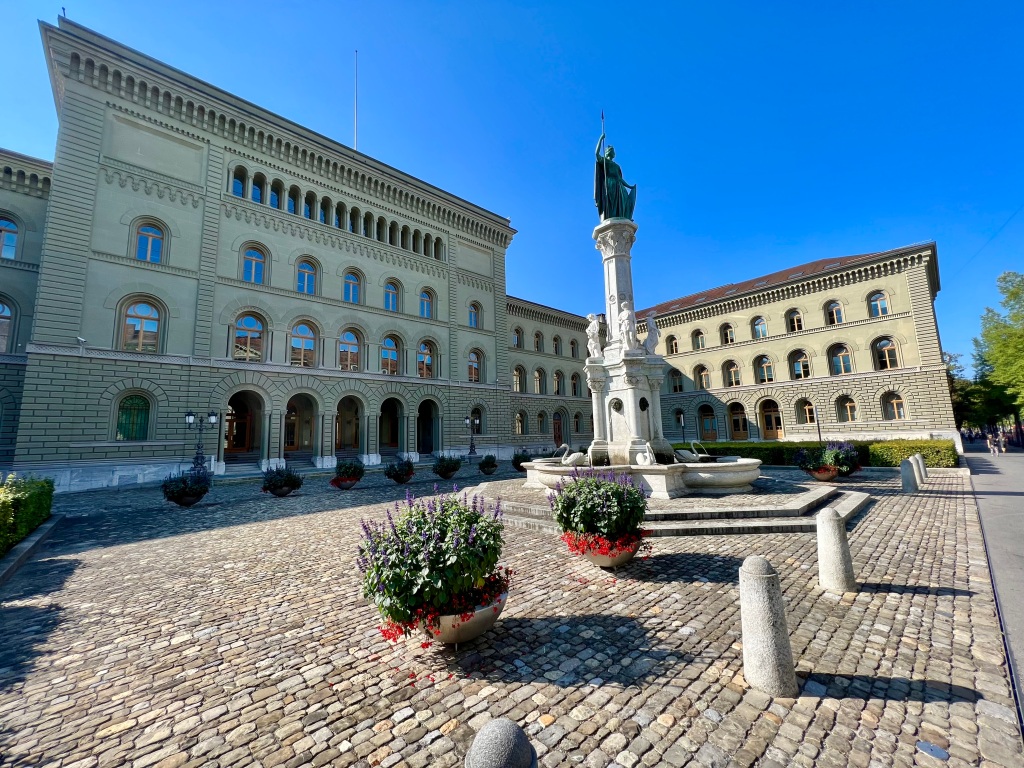 The statute in front of a grand government building, surrounded by a cobbled area.
