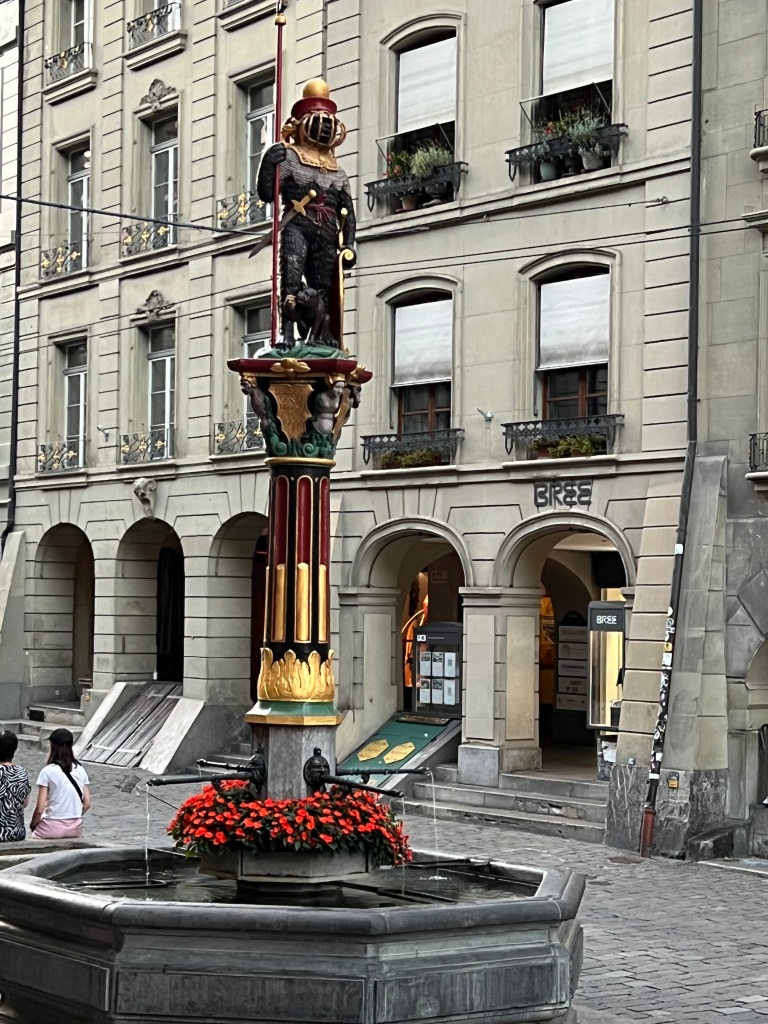 One of the many fountains in Bern with a strange black statute of an ancient warrior wearing a gold coloured face plate.