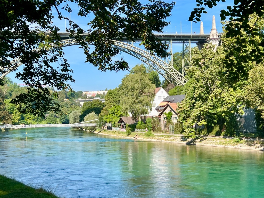 A sunny photo of the river running through the centre of Bern. The water looks a bright green/blue colour.