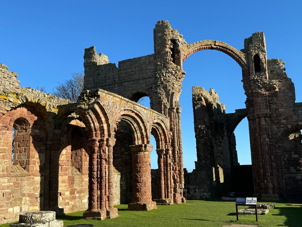 ruins of lindisfarne priory: arches and walls, set against blue sky.