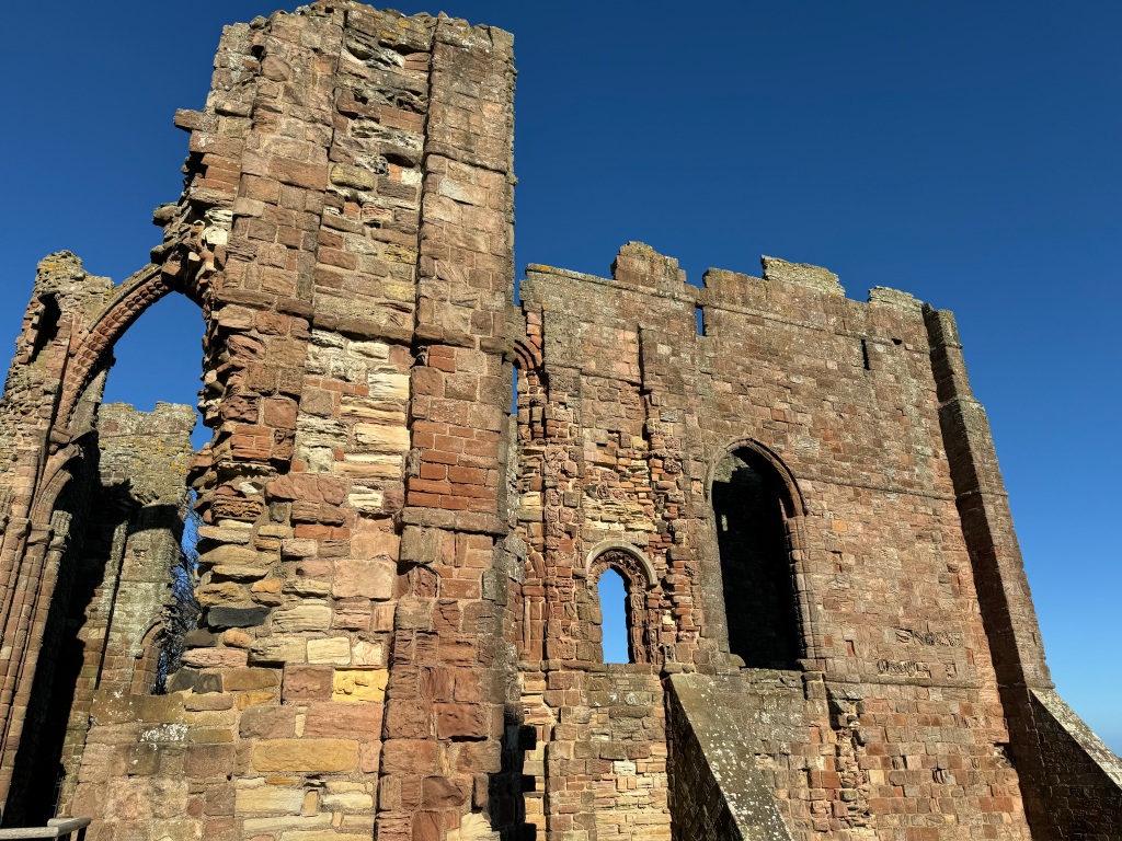 More ruins of lindisfarne priory: arches and walls, set against blue sky.