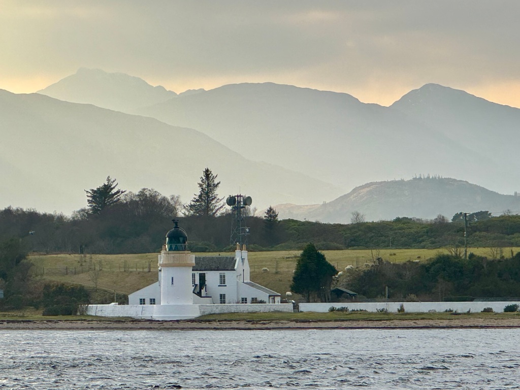 Lighthouse on shore with washed out mountains in background and a yellowish sky