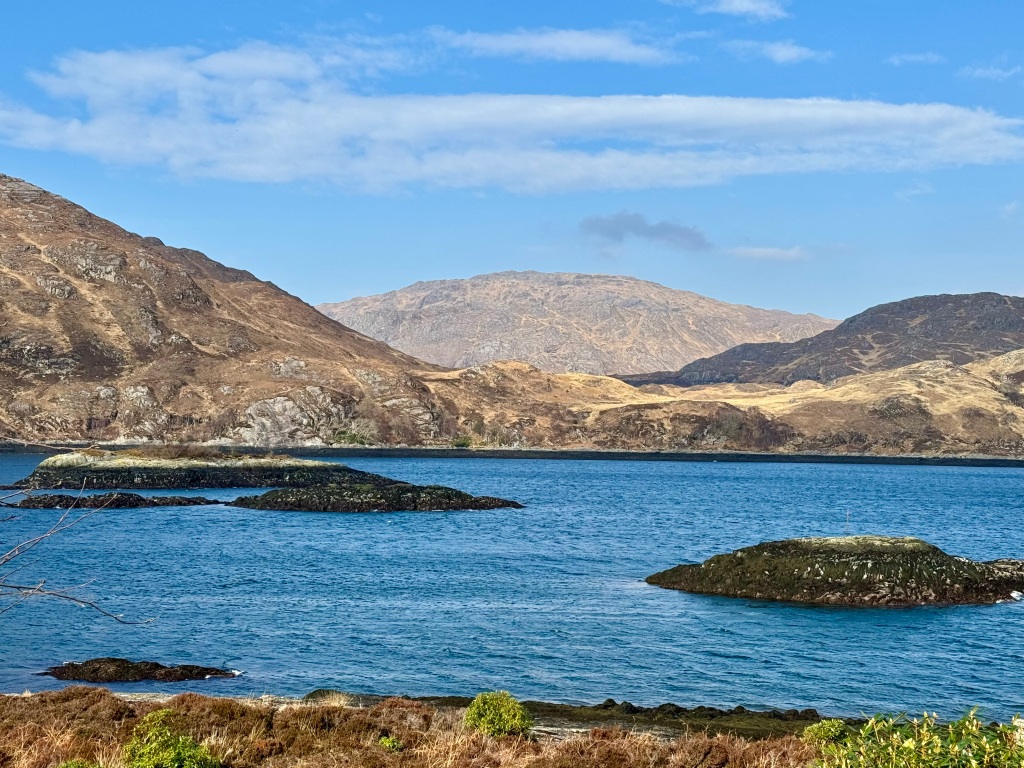 Blue water of loch, with hills in background and rocks in foreground 