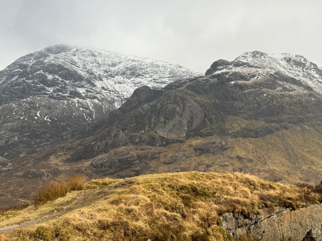 two mountain peaks in Glencoe with a layer of snow near the top.