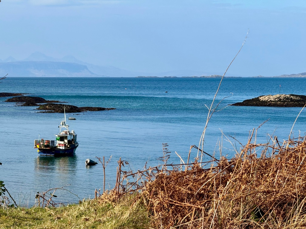 Fishing vessel on deep blue sea, blue sky and a faint outline of mountains on the distant shore.